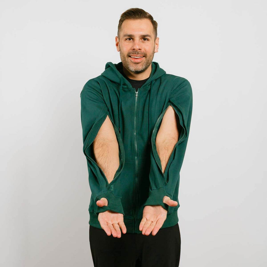 Man wearing dark green zip hoodie with large cutout holes on sleeves against white background.