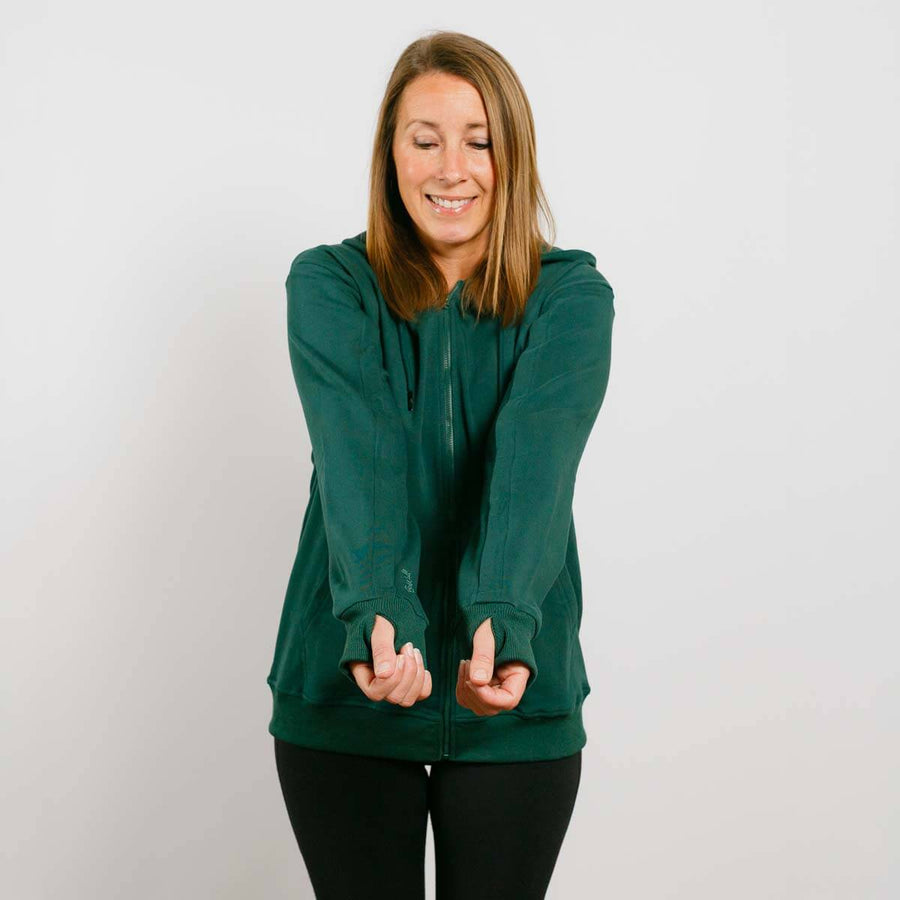 Woman wearing a dark green zip-up hoodie and black pants smiling at camera.