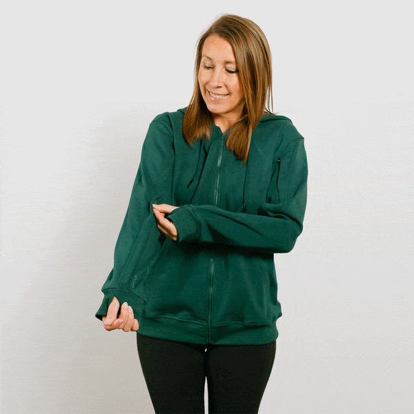 Woman wearing a dark green zip-up hoodie and black pants against a white background.