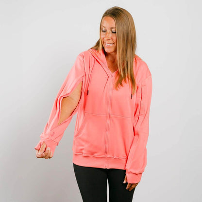Woman wearing a coral pink hoodie with cut-out sleeves on a gray background   | Model is 5'3" 130lbs wearing size S