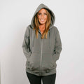 Woman wearing gray zip hoodie with hood up, front view, hands in pockets.