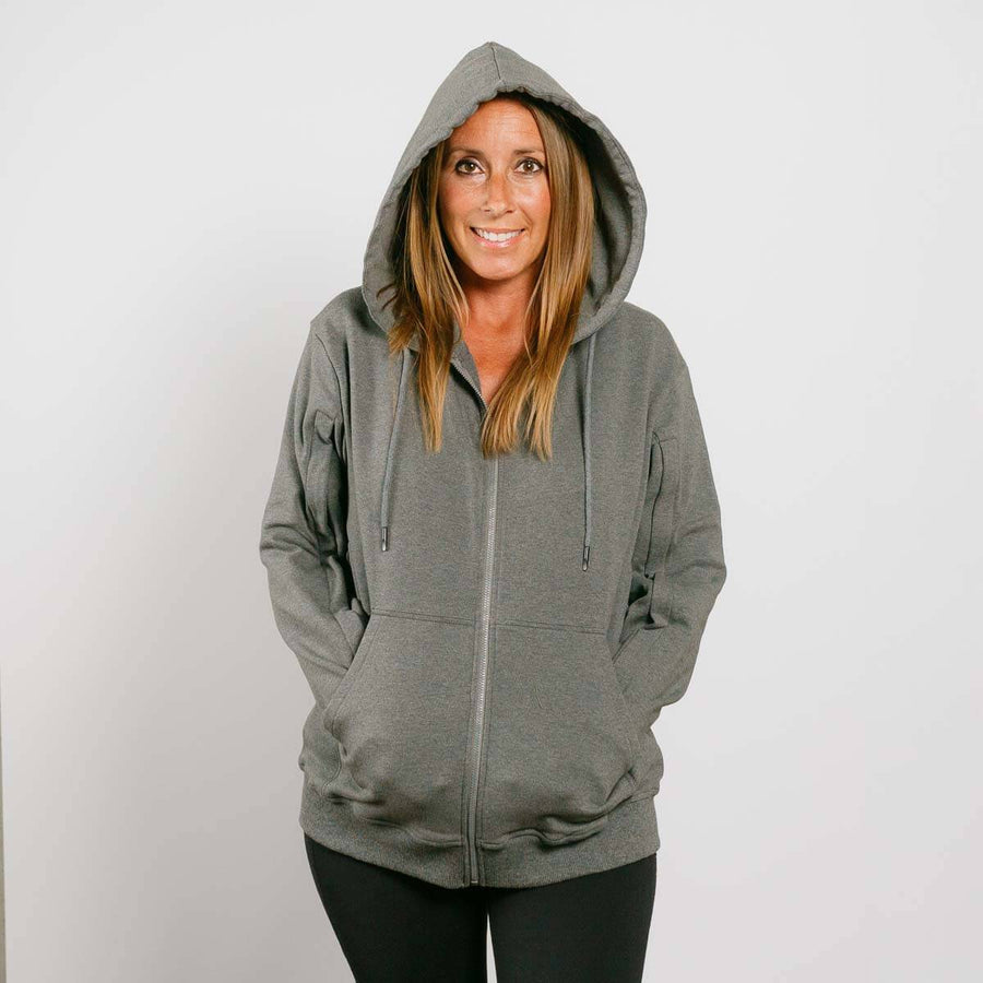Woman wearing gray zip hoodie with hood up, front view, hands in pockets.