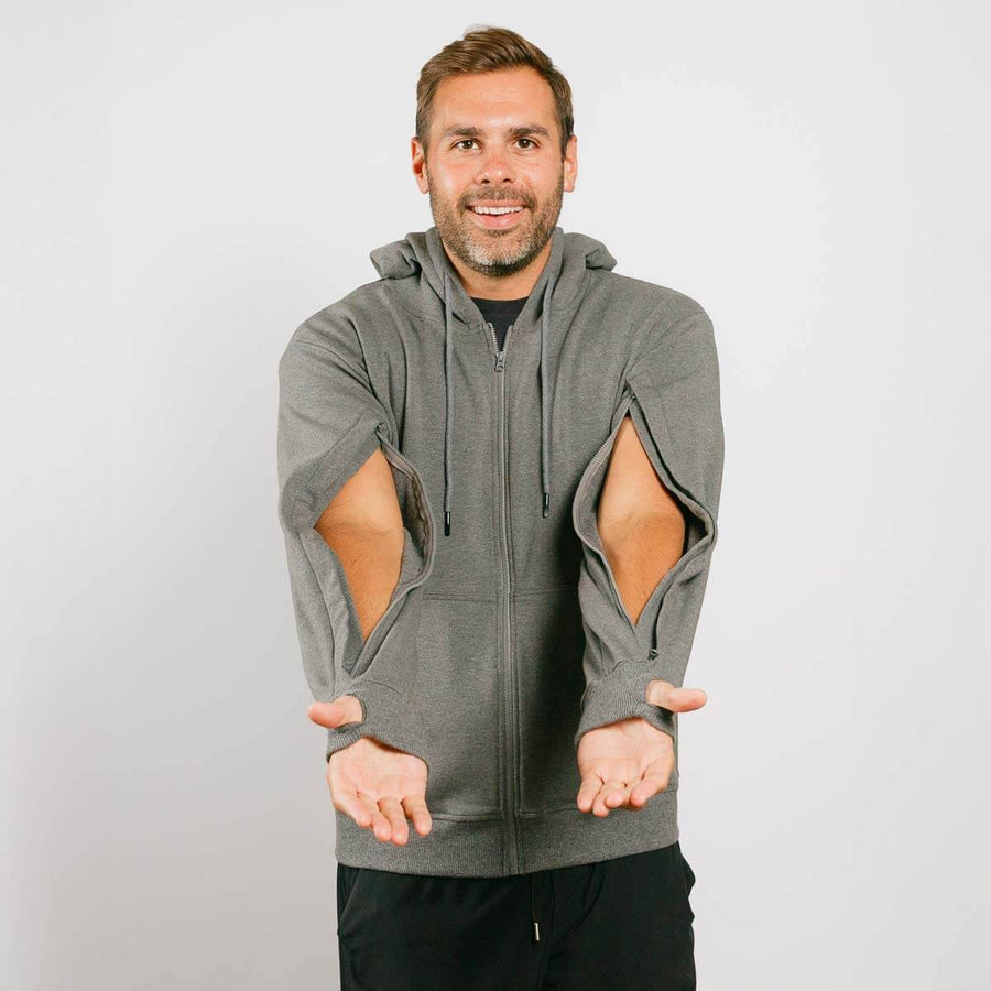 Man wearing gray zip hoodie with large cutout openings on the sleeves, demonstrating the garment's design.