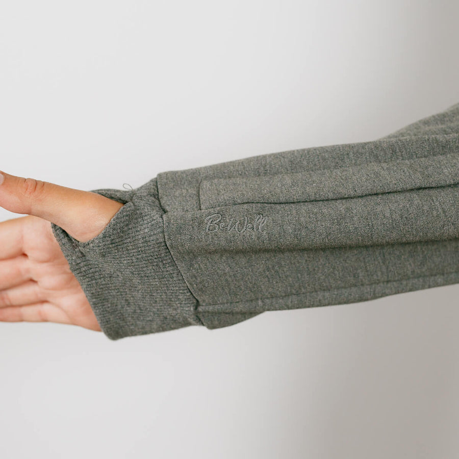 Person wearing sage green IV zip hoodie with left sleeve zipper access feature visible.