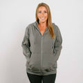 Woman wearing gray zip hoodie with front zipper, standing against white background.