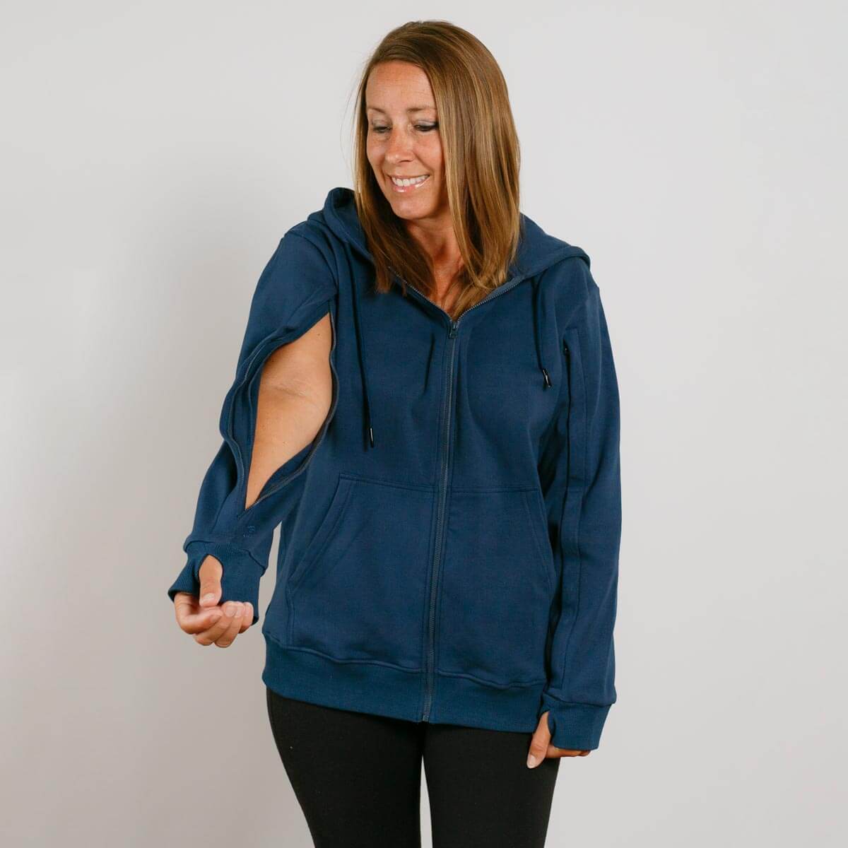 Woman wearing navy blue zip hoodie with open sleeve cutout, smiling while looking down. | Model is 5'3" 130lbs wearing size S