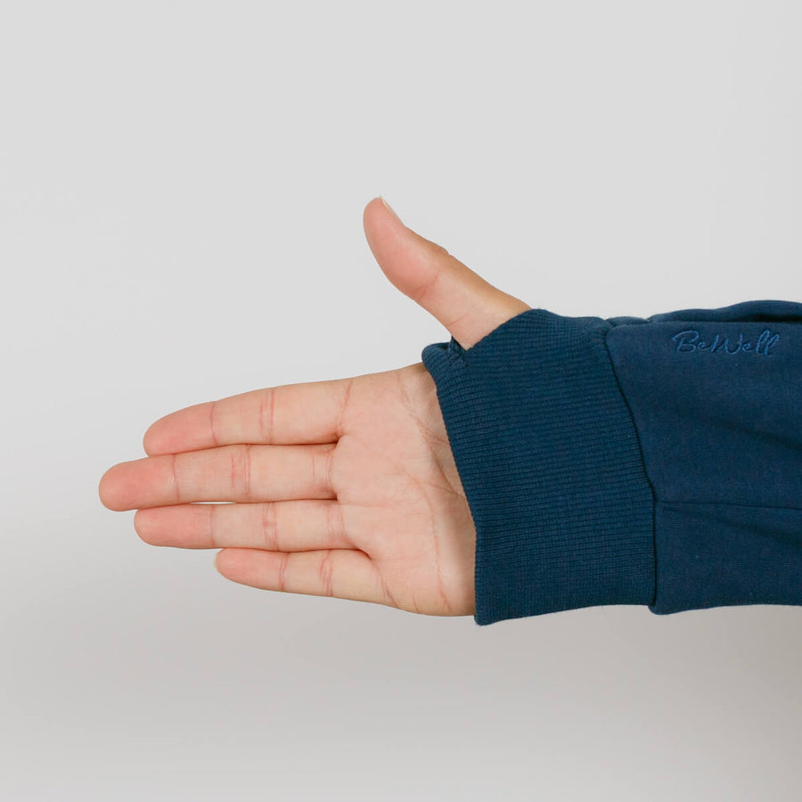 A person's hand extended outward wearing a dark blue zip hoodie with ribbed cuff against a light gray background.