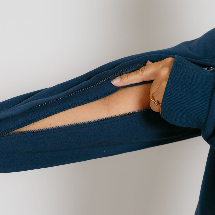 Person wearing navy blue zip hoodie with hand inserted through open side seam pocket.