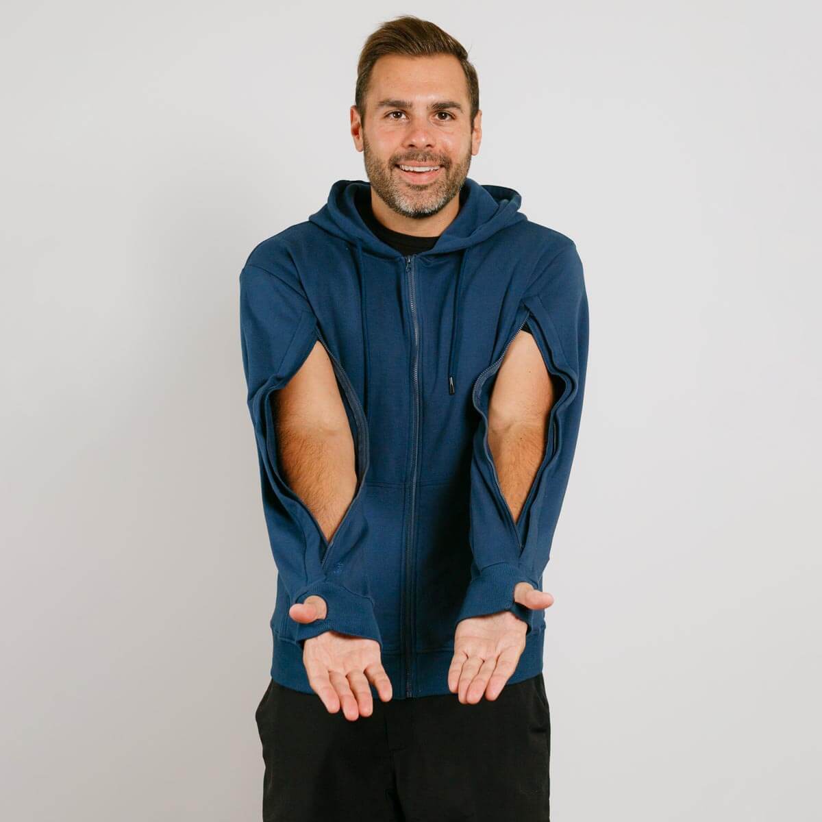Man wearing navy blue zip hoodie with large elbow cutouts over black pants, smiling at camera. | Model is 5'8" 165lbs wearing size M