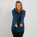 Woman wearing a navy blue zip-up hoodie with black pants, smiling with hands gesturing outward.