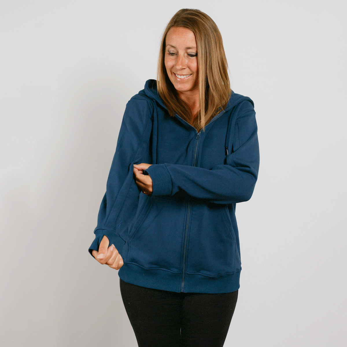 Woman wearing navy blue zip-up hoodie with black pants, smiling and looking down. #gif
