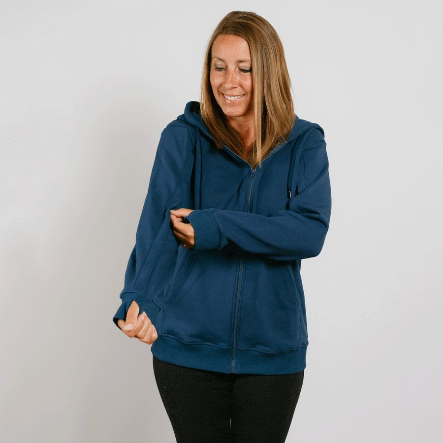 Woman wearing navy blue zip-up hoodie with black pants, smiling and looking down.