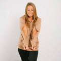 Woman wearing tan IV zip hoodie with front zipper open, smiling downward in lifestyle pose.