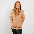 Woman wearing tan IV zip hoodie with front zipper, standing against white background.