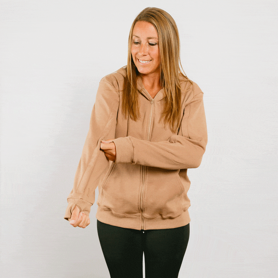 Woman wearing tan IV zip hoodie with front zipper, smiling while adjusting sleeve.