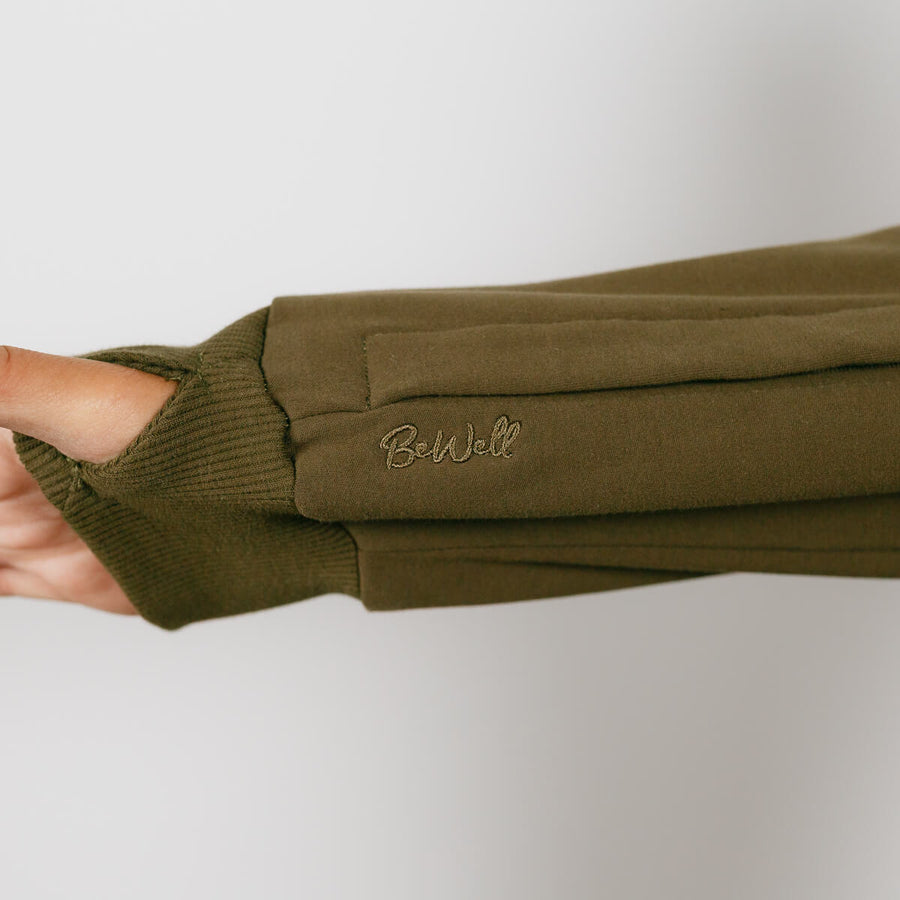 Woman wearing olive green IV zip hoodie with visible left sleeve zipper access detail.