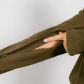 Woman wearing olive IV zip hoodie with left arm zipper partially unzipped for medical access.
