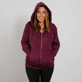 Woman wearing a burgundy zip-up hoodie with hood up and black pants, smiling at camera.