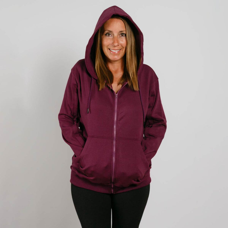 Woman wearing a burgundy zip-up hoodie with hood up and black pants, smiling at camera.