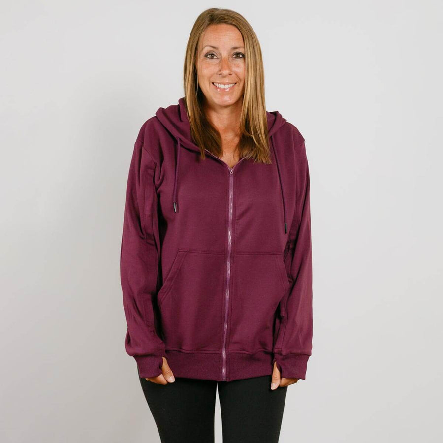 Woman wearing a burgundy zip-up hoodie with black pants smiling at camera.
