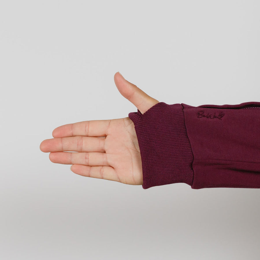 Person's hand extended from a burgundy zip hoodie with ribbed cuff against gray background.