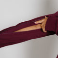 Hand opening the zipper on a burgundy zip hoodie against a white background.