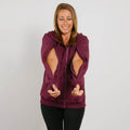 Woman wearing a burgundy zip hoodie with cutout sleeves over black pants, smiling downward.