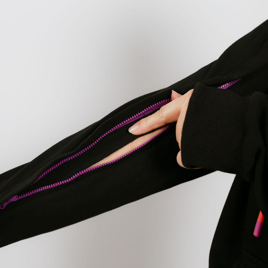 Person wearing black IV zip hoodie with purple zipper showing arm access opening.