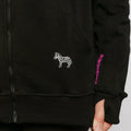 Close-up of black IV zip hoodie showing zebra emblem and purple text detail on sleeve.