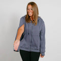 Woman wearing a slate blue zip-up hoodie with black pants, smiling while looking downward.