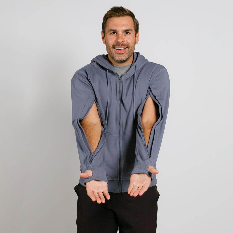 Man wearing a slate blue zip hoodie with open side cutouts, paired with black pants.