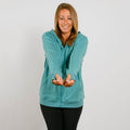 Woman wearing a turquoise zip-up hoodie over black pants, smiling at the camera.