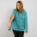 Woman wearing a turquoise zip-up hoodie with black pants against a white background.