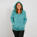 Woman wearing a turquoise zip-up hoodie with black pants, smiling at camera.