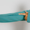 Hand holding turquoise zip hoodie sleeve, showing zipper detail and ribbed cuff against white background.