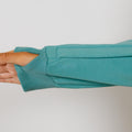A person's arm extends through a turquoise zip hoodie sleeve against a neutral background.