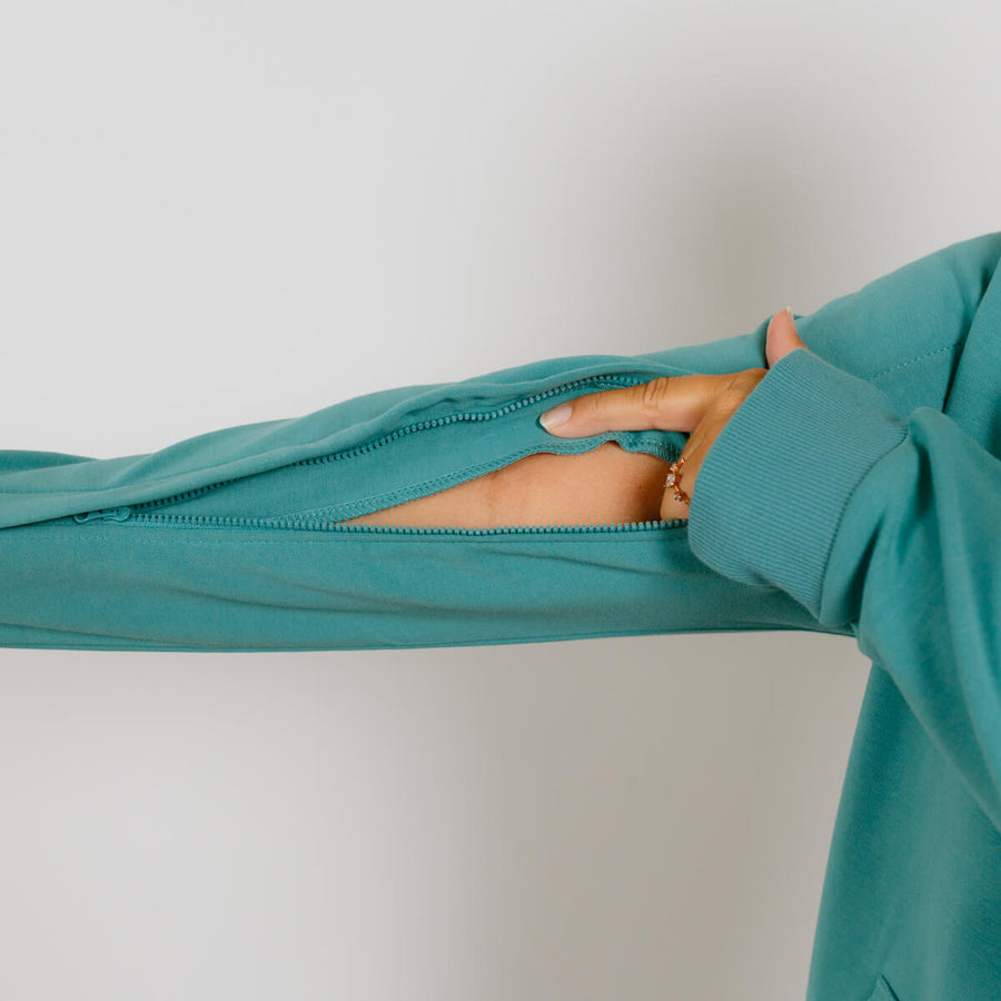 Turquoise zip hoodie displayed flat with sleeve unzipped, showing interior lining and gold bracelet on wrist.