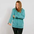 Woman wearing a turquoise zip-up hoodie and black pants smiles while looking downward.