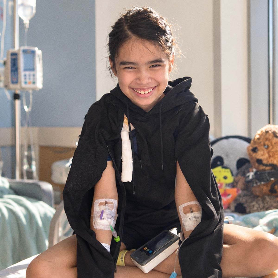 Little girl wearing a black BeWell adaptive hoodie with IV access during treatment in a hospital room