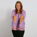 Woman wearing lavender zip hoodie with large cutout holes on the sides and arms, smiling downward.