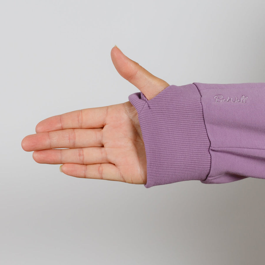 Hand extended from purple hoodie sleeve with ribbed cuff against neutral background.