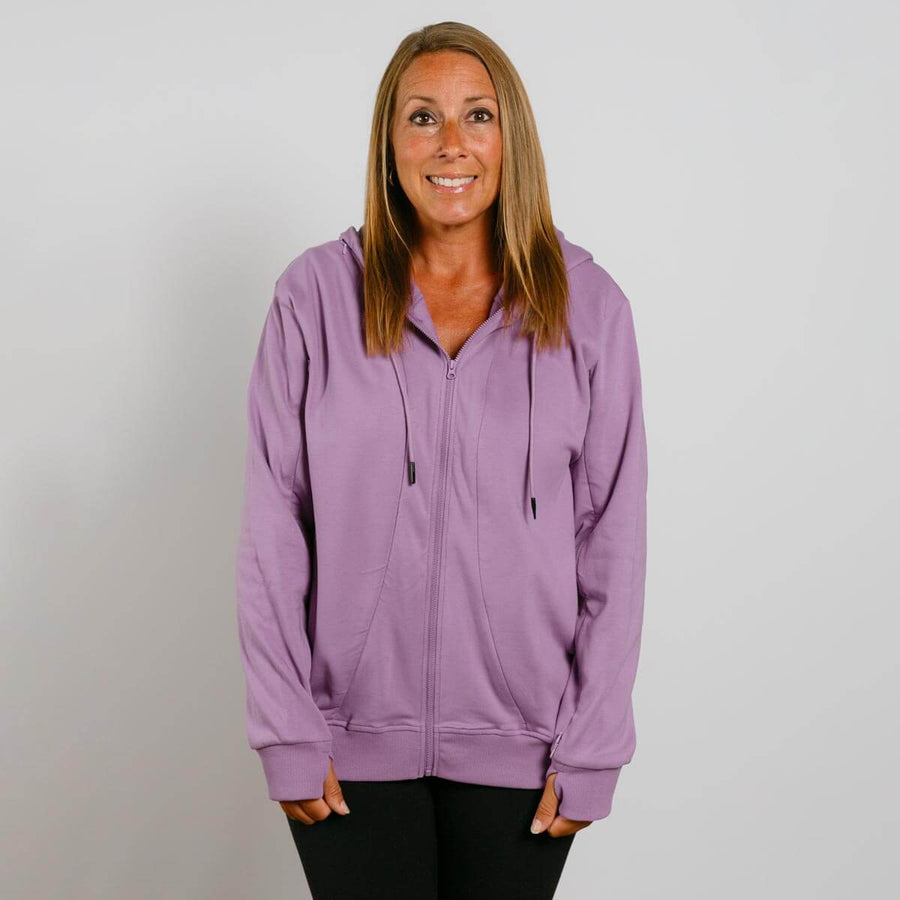 Woman wearing a purple zip-up hoodie with drawstrings over black pants against a white background.