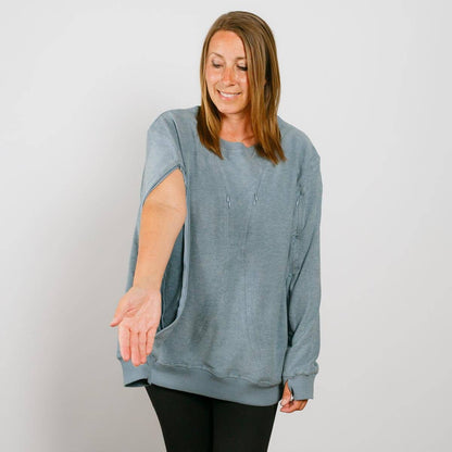 Woman wearing a blue-gray crewneck sweatshirt with an open side seam, paired with black pants.