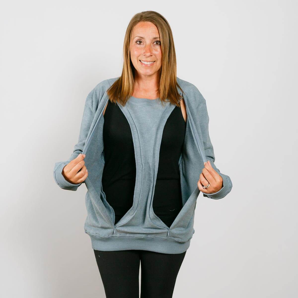 Woman wearing light blue zip-up crewneck sweatshirt over black shirt and black pants, smiling at camera. | Model is 5'3" 130lbs wearing size S