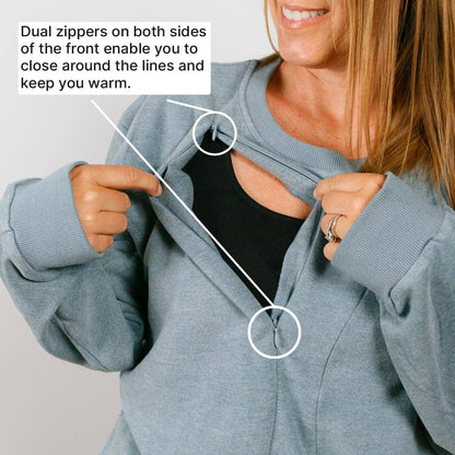 Woman demonstrates dual front zippers on light blue crewneck sweatshirt opening from both sides.