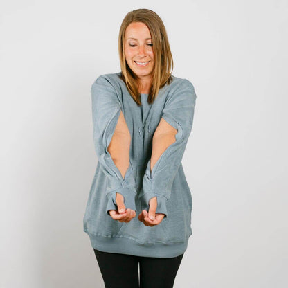 Woman wearing a light blue distressed crewneck sweatshirt with elbow cutouts and black leggings.