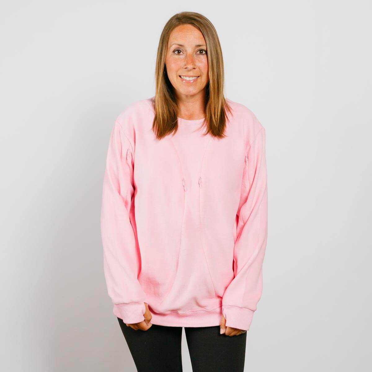 Woman wearing a pink crewneck sweatshirt and black pants smiling at camera.