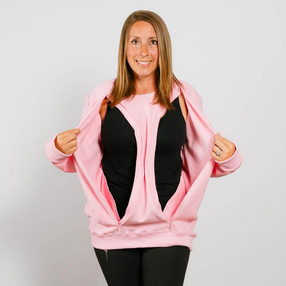 Woman wearing pink zip-up crewneck over black shirt and black pants, smiling at camera. | Model is 5'3" 130lbs wearing size S