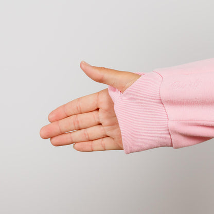 Hand in pink crewneck sweatshirt with ribbed cuff displayed against neutral background.
