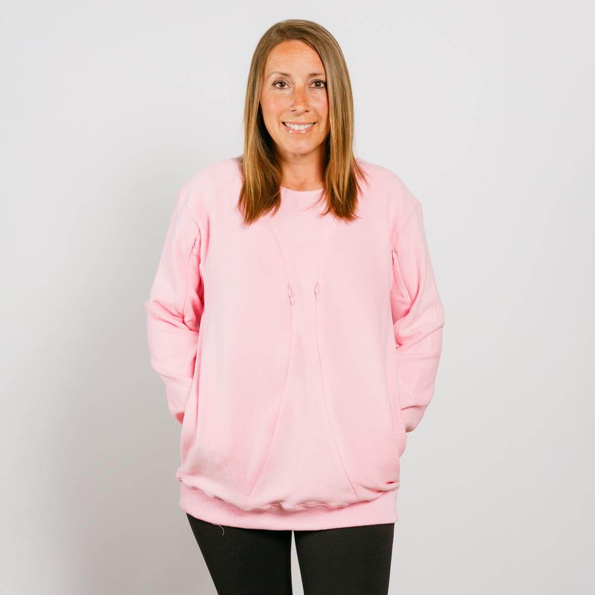 Woman wearing a pink crewneck sweatshirt with long sleeves and black pants, smiling at camera.